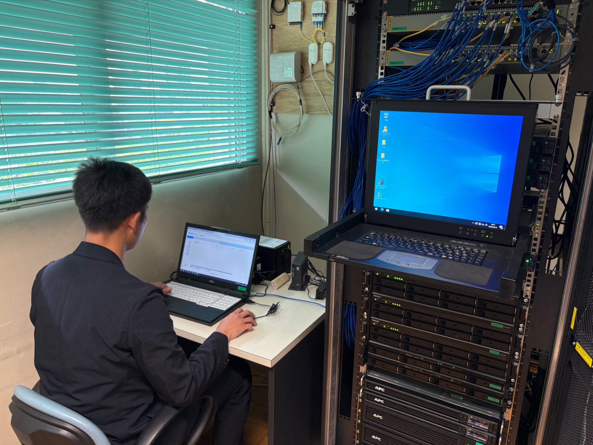 『Yubi Plus』の管理画面で設定変更を行う高橋様、右はラックマウント型サーバー(2Uサイズの認証サーバー)